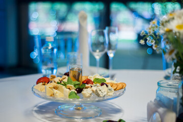 Glass plate with appetizers on the banquet table. Cheeses, walnuts, honey, grapes, mint leaves