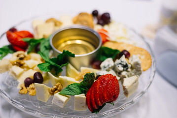 Glass plate with appetizers on the banquet table. Cheeses, walnuts, honey, grapes, mint leaves