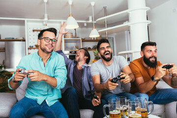 Smiling male friends with gamepads and beer playing video game at home