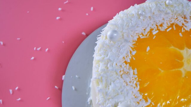Cake with orange and coconut shavings spun on a pink background.