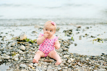 Outdoor portrait of adorable baby girl playing with seaweed by the river, wearing pink swimsuit