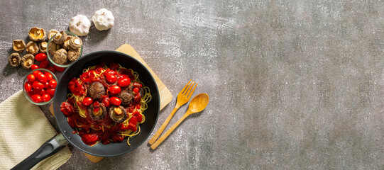 spaghetti,Spaghetti and sauce in a frying pan are sprinkled with cheese and fresh basil on a background of spices and onions on a black concrete background 