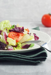 Salad with tomatoes, leaves in a plate on the table. There is a cotton towel under the plate