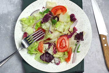 Salad with tomatoes, leaves in a plate on the table. There is a fork and a knife nearby. There is a towel under the plate