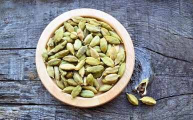 Green cardamom pods on a wooden plate on vintage wooden background.Elettaria cardamomum seeds.Organic herbs and spices concept.Selective focus.