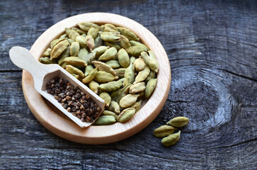 Green cardamom pods and seeds on a wooden plate on vintage wooden background.Elettaria cardamomum.Organic herbs and spices concept.Selective focus.