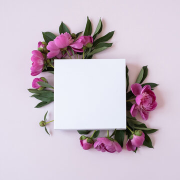 Wreath made of elegant pink peonies flowers with blank mockup copy space paper sheet on pastel pink background. Flat lay, top view brand, blog, website, social media template