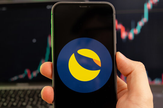 Terra LUNA cryptocurrency logo on the screen of a smartphone in mans hand with a growing trend on the chart on a green background.
