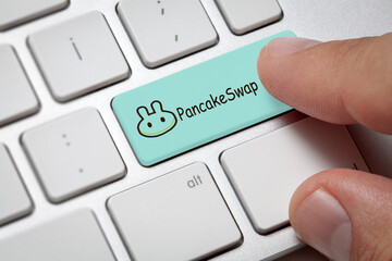 Index finger pressing computer key with pancakeswap altcoin logo. Cryptocurrency concept.
