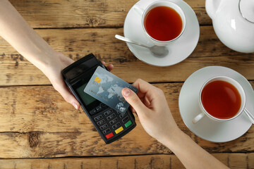 Woman with credit card using modern payment terminal at wooden table, top view - obrazy, fototapety, plakaty