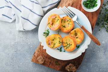Egg muffins with green onions, bacon, cheese and tomatoes on white plate on light background. Healthy high protein and low carb breakfast, ready to eat.