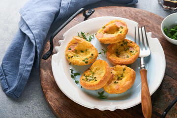 Egg muffins with green onions, bacon, cheese and tomatoes on white plate on light background. Healthy high protein and low carb breakfast, ready to eat.
