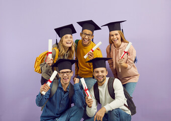 Happy multiracial students show their certificates while posing on purple background. Students in...