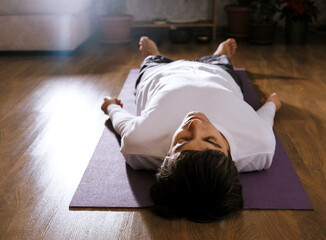 Man is lying on floor on yoga mat in shavasana pose. Concept of yoga and relaxation.