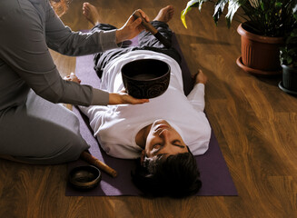 Woman making relaxing massage for young man.  Meditation, sound therapy with Tibetan singing bowls.