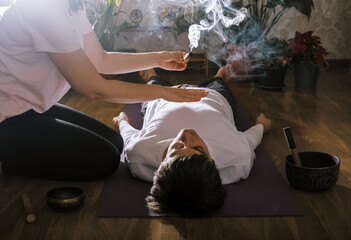 Woman holds incense over  man lying on  yoga mat. Esoteric massage concept.