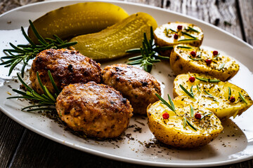 Roast meatballs with boiled potatoes and pickled cucumbers on wooden table
