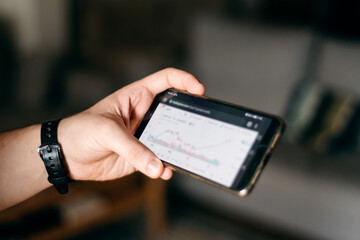 Young male holding his cellphone with graphic chart of the stock market
