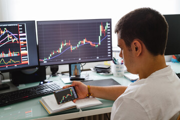 Successful young trader in casual wear working with charts and market reports at home