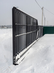 Close-up of a sliding metal gate made of a gray picket fence in winter. Protection of the...