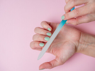 a woman herself is filing her nails with a nail file on her hand on a pink background. Hand nail care at home. Beauty and Health