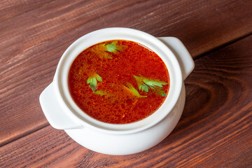 Close-up of soup borscht in a white ceramic soup bowl on a wooden background. Traditional soup for Russia and Ukraine. Greens float on top of the soup. Top view