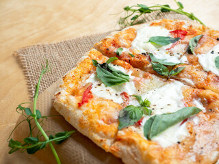 Close-up of a fresh hot Roman pizza with tomatoes and strachatella cheese on a raw wooden background. Italian cuisine, linen napkin.