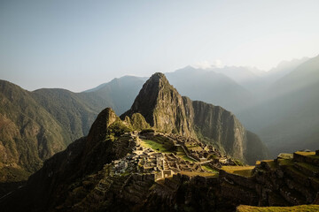 Fototapeta na wymiar World-famous Inca city of Machu Picchu during sunrise with yellow light rays and misty clouds (without any visitors) (Aguas Calientes, Peru, South America)