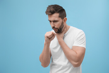 Man coughing on light blue background, space for text. Cold symptoms
