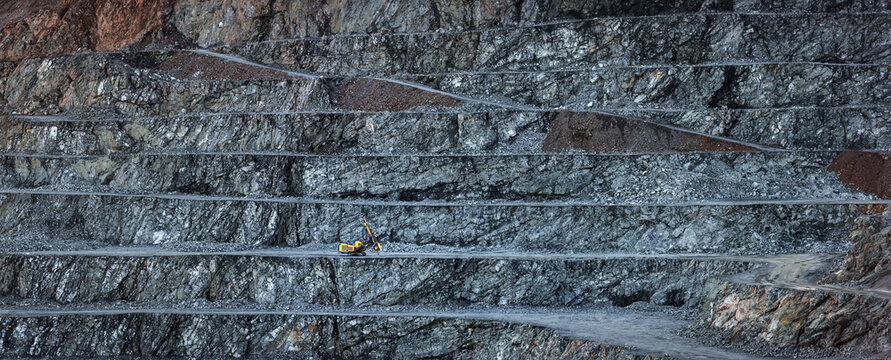 Panorama of diabase quarry with stepped wall and one yellow drilling machine on a bench