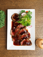 Beef carpaccio on a white plate with sauce and herbs on a wooden background. Top view with a space...