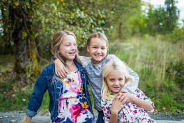 Three best friends laugh, hug and smile outside.