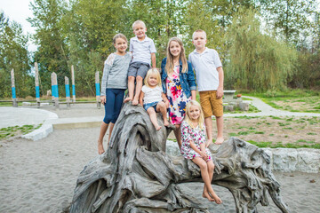 Portrait of barefoot kids playing on large stump at park.