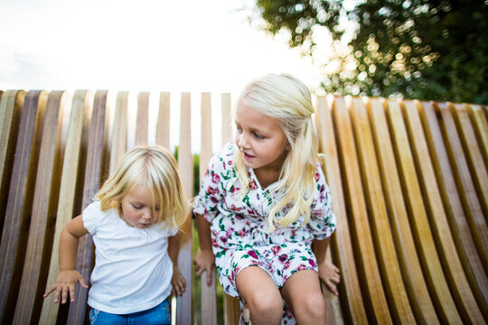 Sisters playing on wooden bench outdoors.