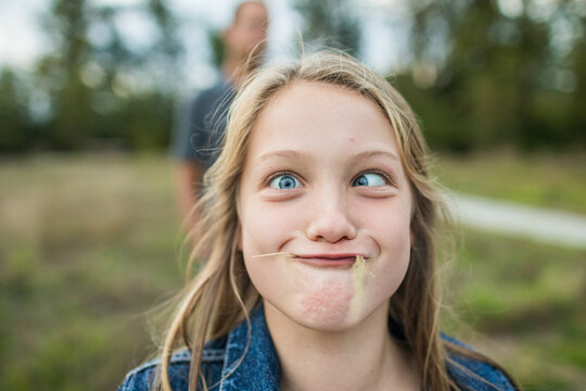 Young girl makes sill face, crazy eyes, grass in mouth.
