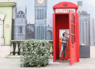 A boy and a girl are playing near a red telephone booth