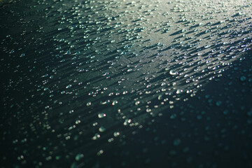 Close up shot of the beautiful raindrops in sunlight on the dark aquamarine surface. Drops on the rain cover waterproof fabric. Abstract Water droplets for wallpaper, backgrounds, poster, backdrop.