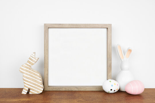 Mock up wood frame with Easter egg and bunny decor on a wood shelf against a white wall. Copy space.