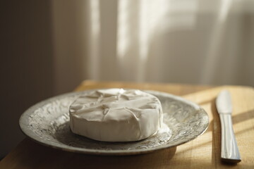 Whole round Camembert cheese on a silver plate with a knife on wooden table