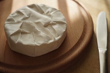 Whole round Camembert cheese with a knife on wooden boards