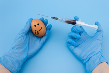 The syringe is injected into the egg close-up on a blue background. The topic of vaccination of...
