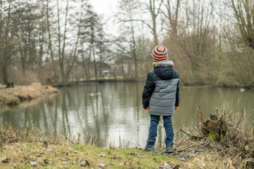 Fototapeta na wymiar Ein kleines Kind steht in Winterjacke an einem großen Teich