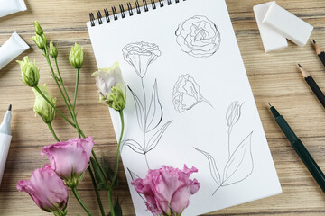 Sketches of flowers in notebook, eustomas and art supplies on wooden table, flat lay