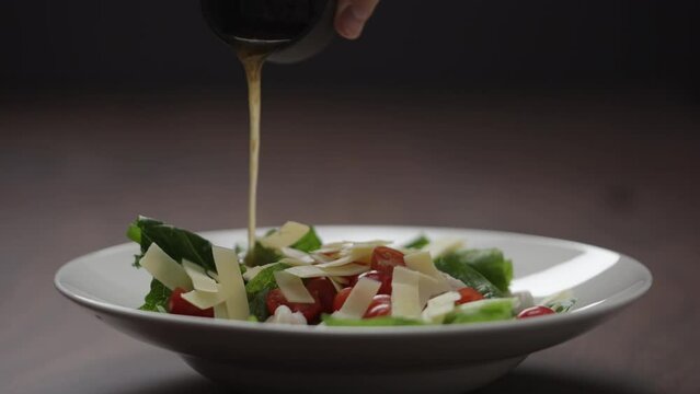 Slow motion man making salad pour dressing over in white bowl