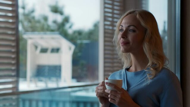 The beautiful woman standing by the window with a cup of coffee. slow motion
