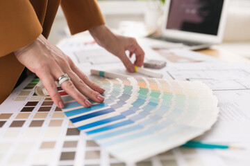 Close-up of architect woman choosing samples of wall paint. Interior designer looking at color swatch for creating project. House renovation, architecture and interior design concept. - obrazy, fototapety, plakaty