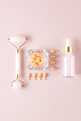 beauty treatment cosmetic set for dayl skin care routine. Single dose serum capsules. brauty oil in dropper bottle and rose quartz massage roller on pink background.