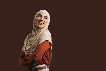 Beautiful muslim woman wearing beige hijab, orange blouse and beige pants smiling and looking back...