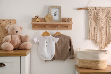 Wooden shelf with baby clothes, toys and furniture in room. Interior design
