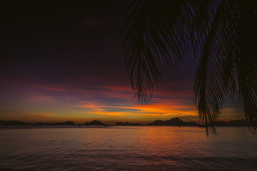 Naklejka na ściany i meble Picturesque tropical sunset. Dramatic evening sky above island. Palm tree and isles silhouettes. Exotic seascape in evening twilight. El Nido lagoon in night dusk. Tropical vacations.
